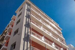 Un immeuble à plusieurs étages, doté de balcons, se dressant sous un ciel d’un bleu limpide.