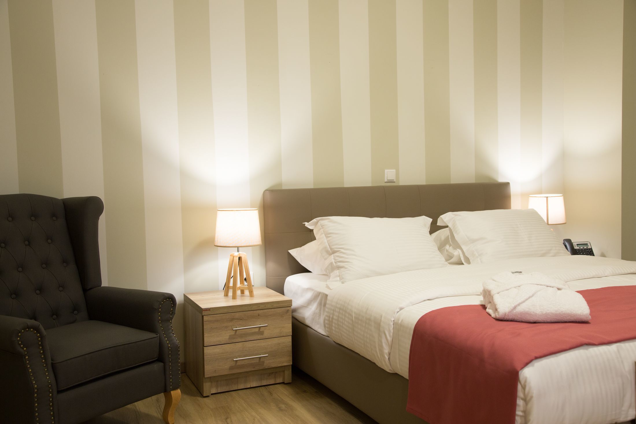 A hotel room with a bed, bedside lamps, a chair, and a nightstand.