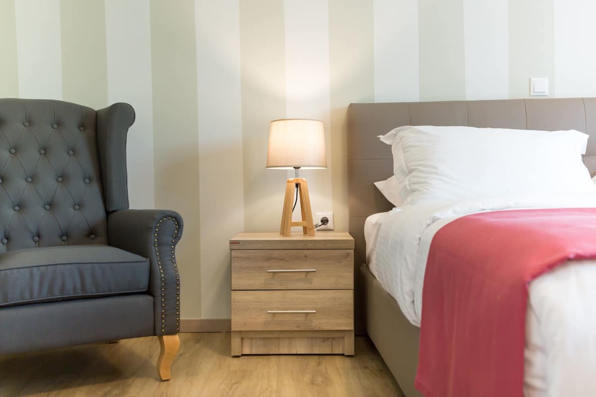 A bedroom with a bed, a nightstand with a lamp, a sofa, and striped wallpaper.