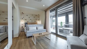 A modern living room with a sofa, a coffee table, and a view of the outdoors through large windows. - Hotel @ Syngrou Fix (Athens)