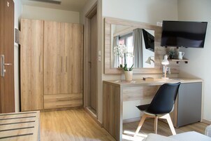 Quarto com guarda-roupa de madeira, escrivaninha com cadeira, televisão e espelho.