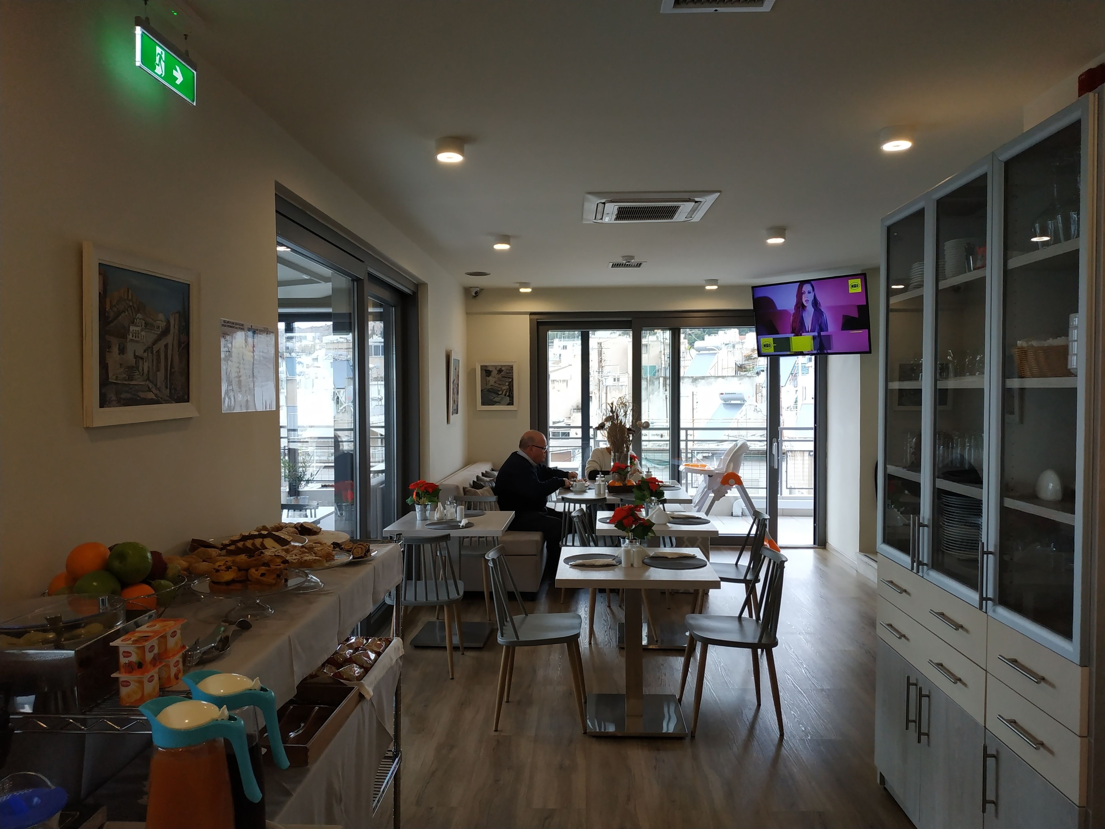 A restaurant with a buffet, dining tables, chairs, and a TV screen.