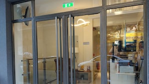 A hotel entrance with a glass door, a fire extinguisher, and a visible interior including a counter and a chair. - Hotel @ Syngrou Fix (Athens)