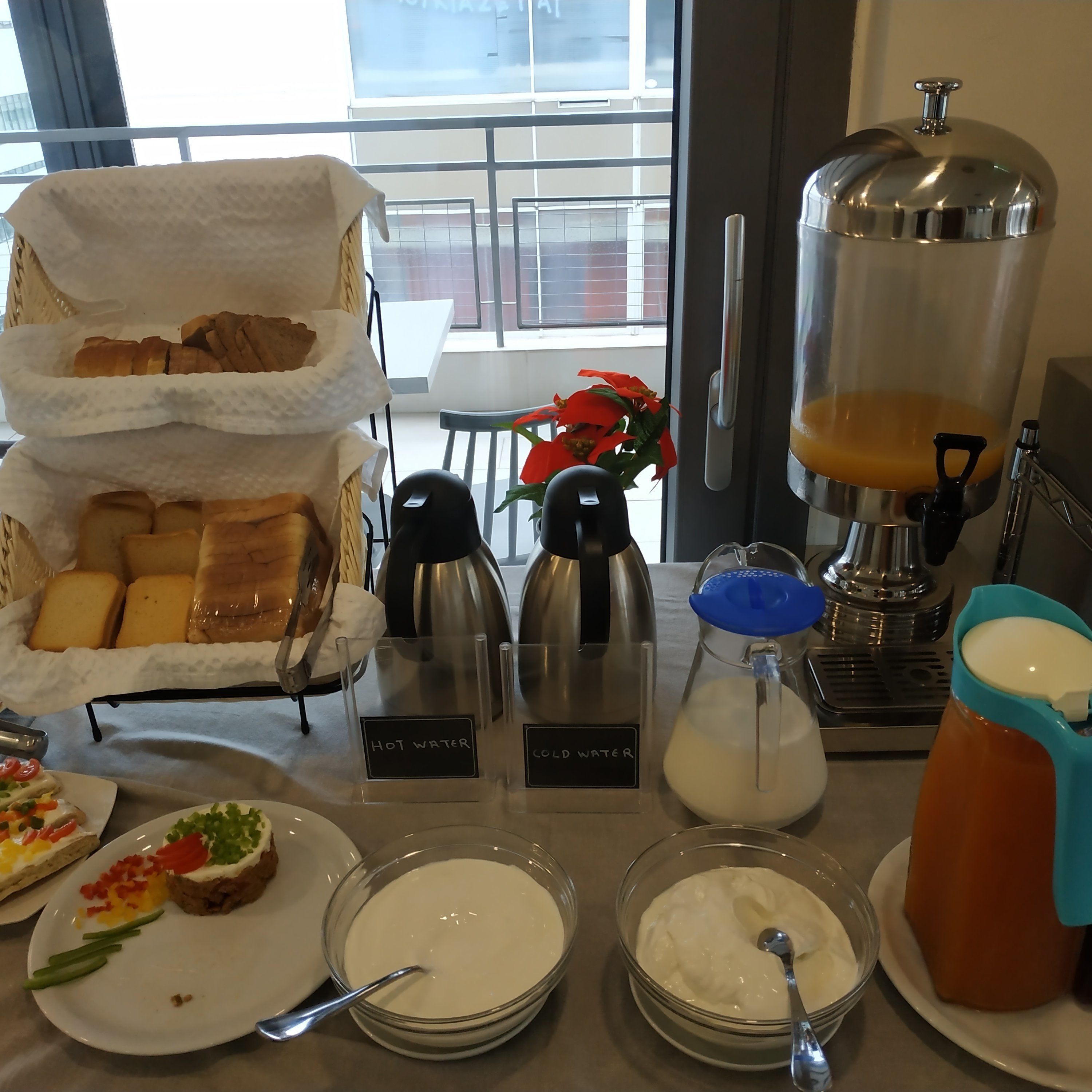 Un bufé de desayuno con pan, agua fría y caliente, café y yogur.