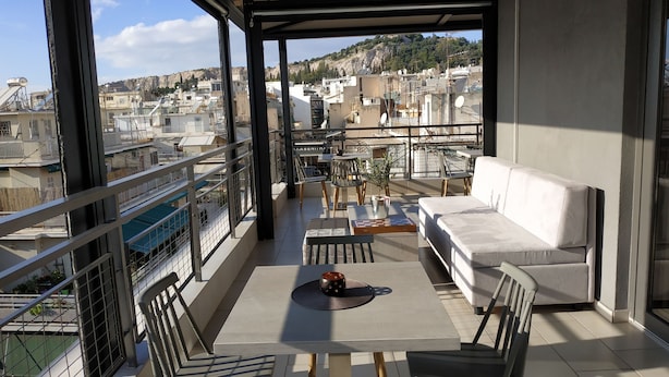 A balcony with a sofa, chairs, a table, and a view of the cityscape. - Hotel @ Syngrou Fix (Athens)