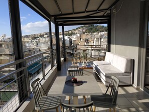 A balcony with a sofa, chairs, a table, and a view of the cityscape. - Hotel @ Syngrou Fix (Athens)