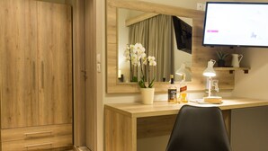A hotel room with a wooden wardrobe, a desk with a chair, a mirror, a potted orchid, a bottle of liquor, and a television. - Hotel @ Syngrou Fix (Athens)