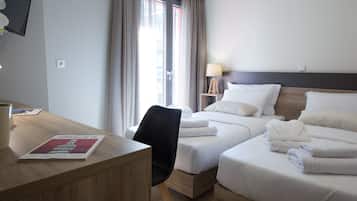 Two single beds with white linens and pillows, a desk, chair, and lamp.