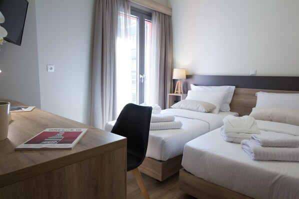 Une chambre d’hôtel avec deux lits, un bureau et une chaise. Il y a une lampe sur le bureau et une affiche au mur.