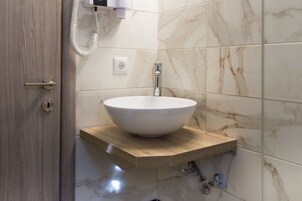 Casa de banho com toucador de madeira, lavatório de mármore branco e telefone fixado na parede.