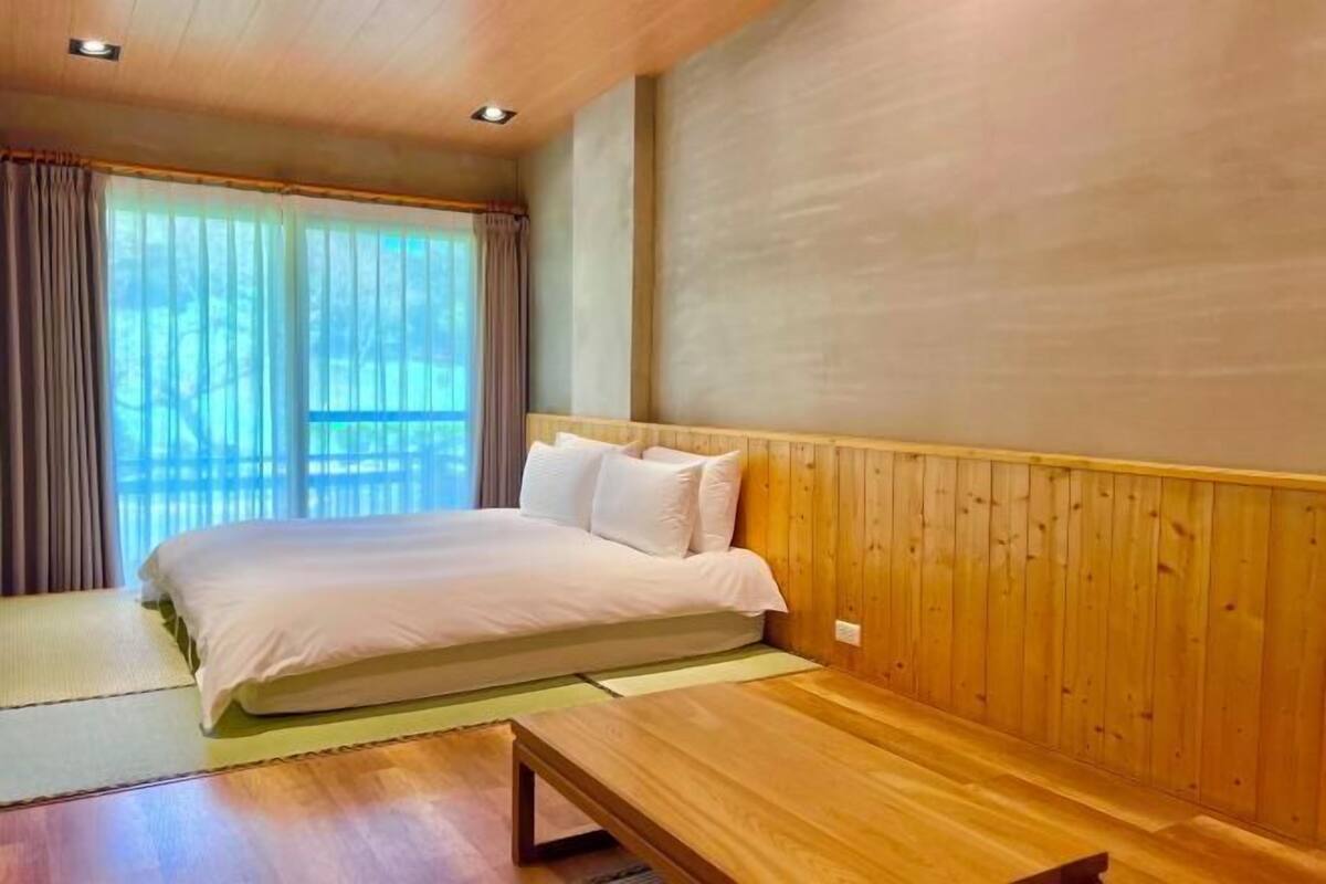 A bedroom with a bed, wooden paneling, a window with curtains, and a wooden bench.