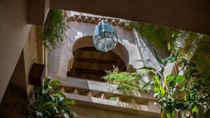 Une fenêtre en arc surmontée d’une lanterne suspendue, le tout entouré de verdure et agrémenté de détails architecturaux.