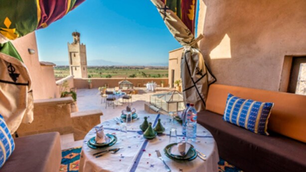 Un coin repas avec une table dressée pour quatre personnes, un canapé avec des coussins et une vue sur une tour au loin.