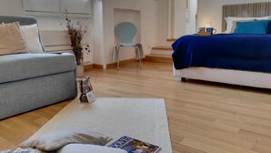 Habitació d'hotel moderna amb un sofà gris, un llit blau i una taula petita amb una revista.