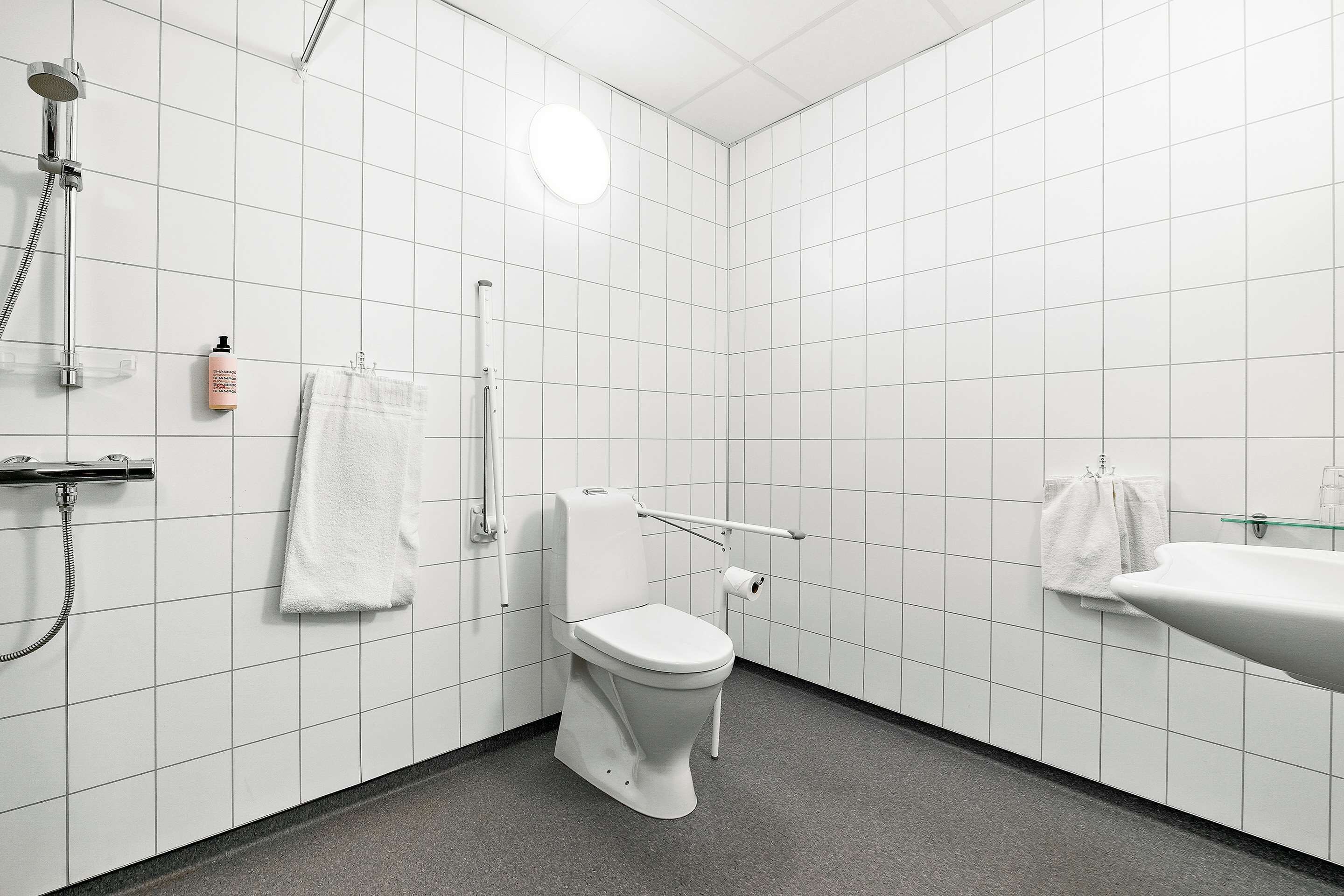 A modern bathroom with white tiles, a white toilet, a shower, and a sink.