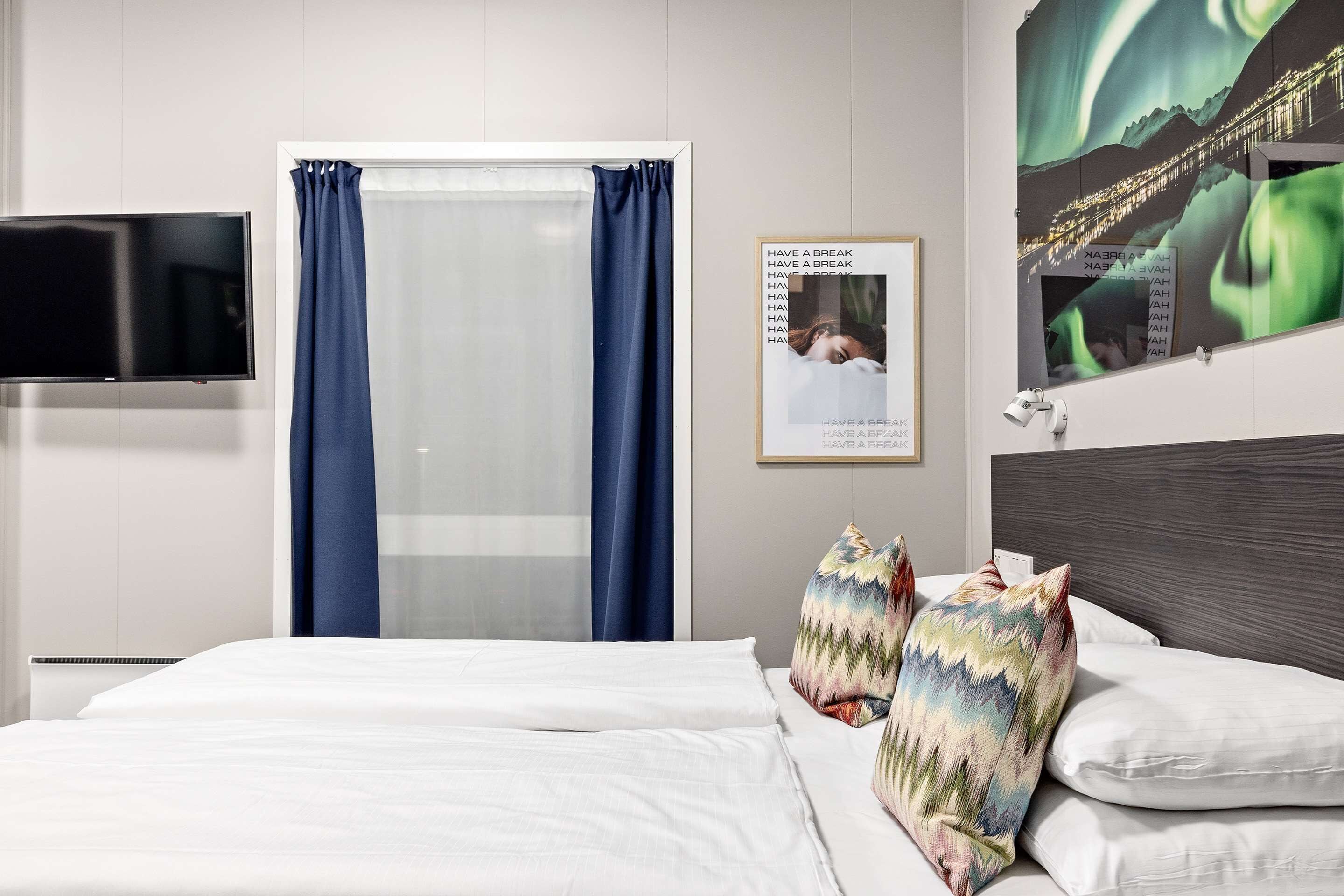 A hotel room with a bed, a TV, a window with curtains, and a poster on the wall.