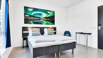 Une chambre d’hôtel moderne, équipée d’un lit, d’un bureau et d’une grande œuvre d’art représentant les aurores boréales, accrochée au mur.