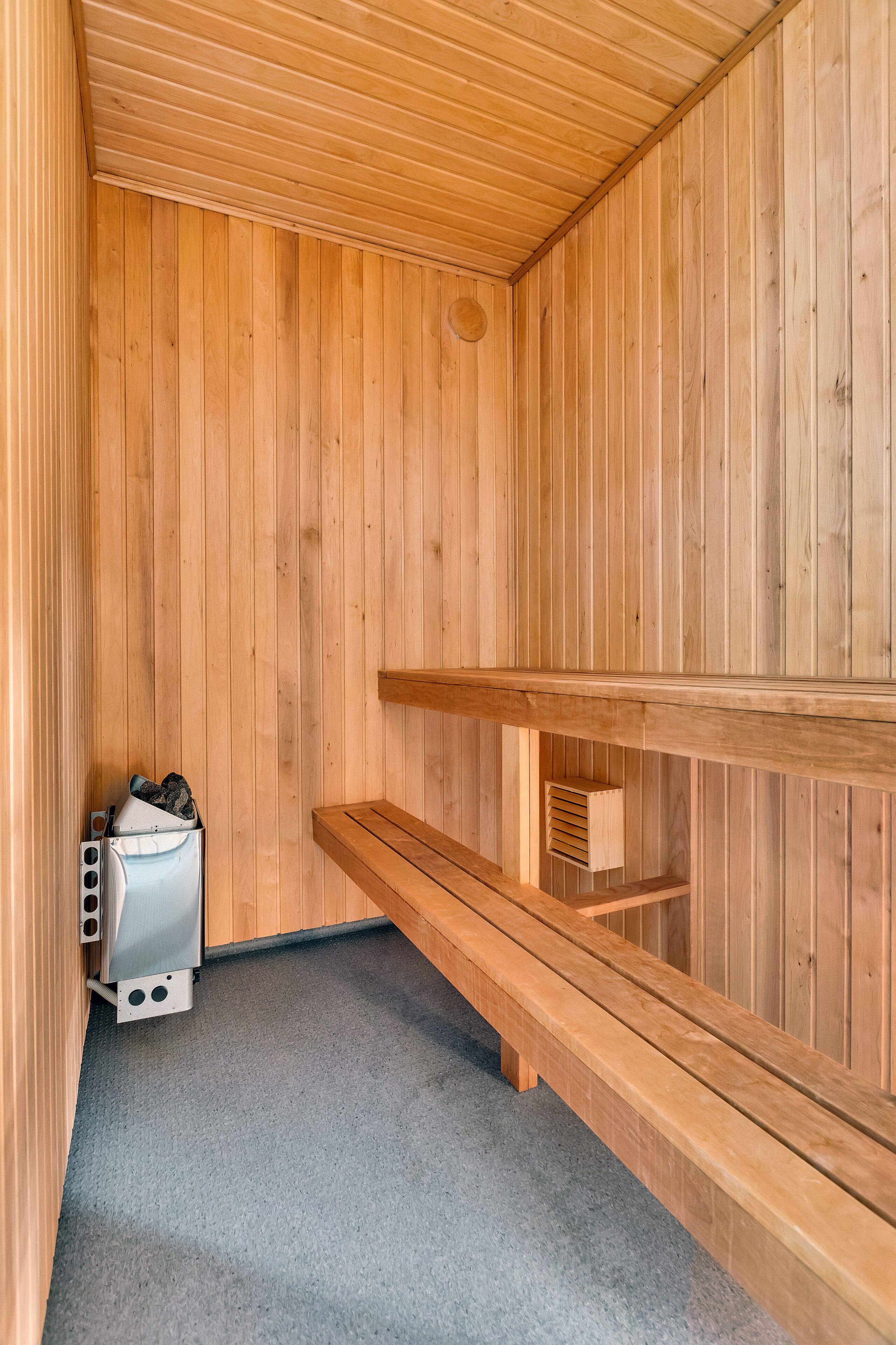 Eine Sauna mit Holzwänden und -bänken, einem Dampfgenerator und einem Lüftungssystem.