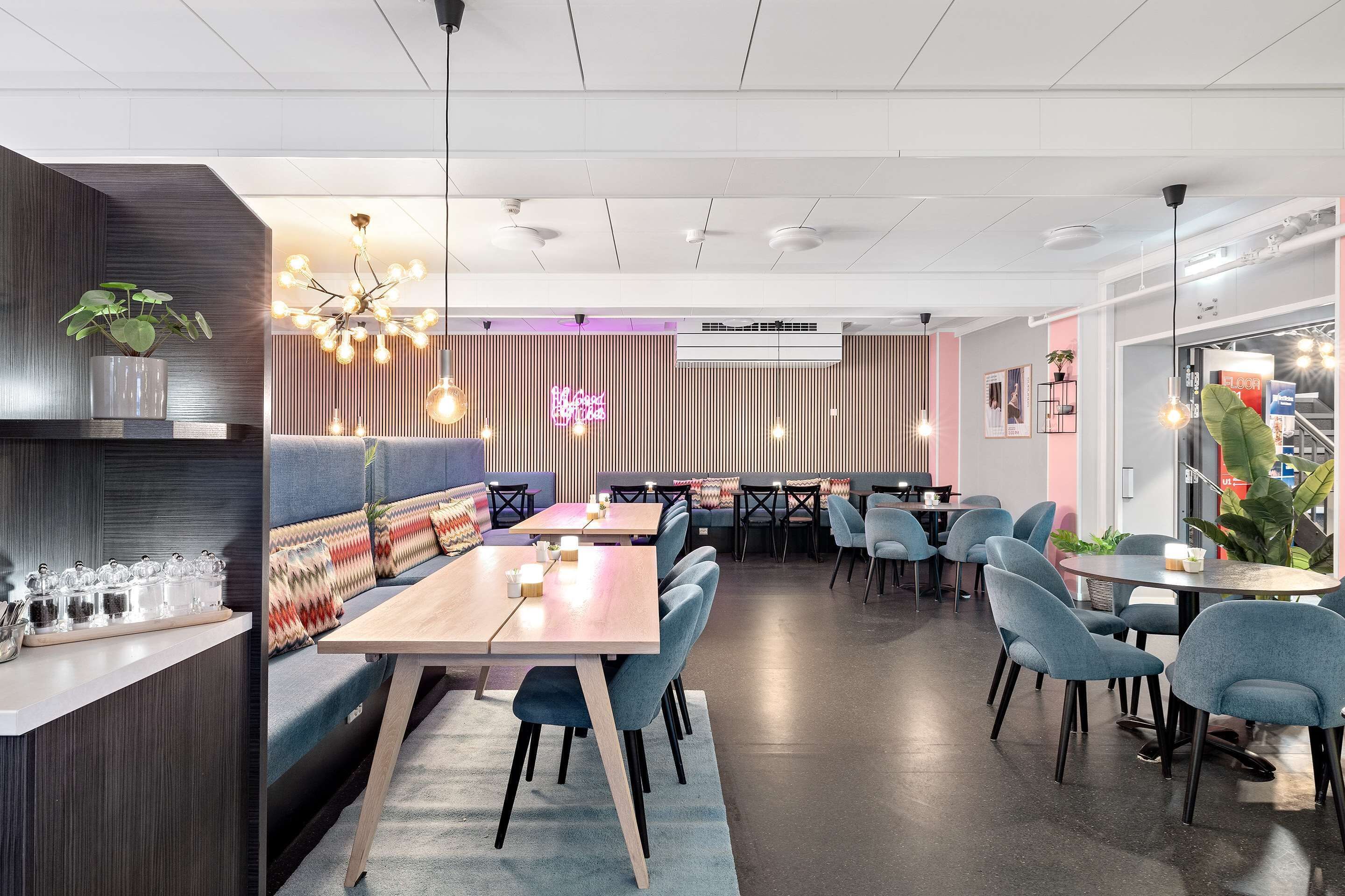 Un restaurante moderno con una zona de asientos tipo cabina de madera, mesas redondas y sillas azules.