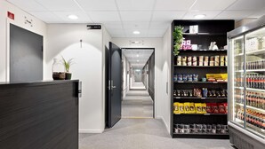 Un pasillo con mostrador de recepción, cartel de sala privada, máquina expendedora y refrigerador con bebidas.