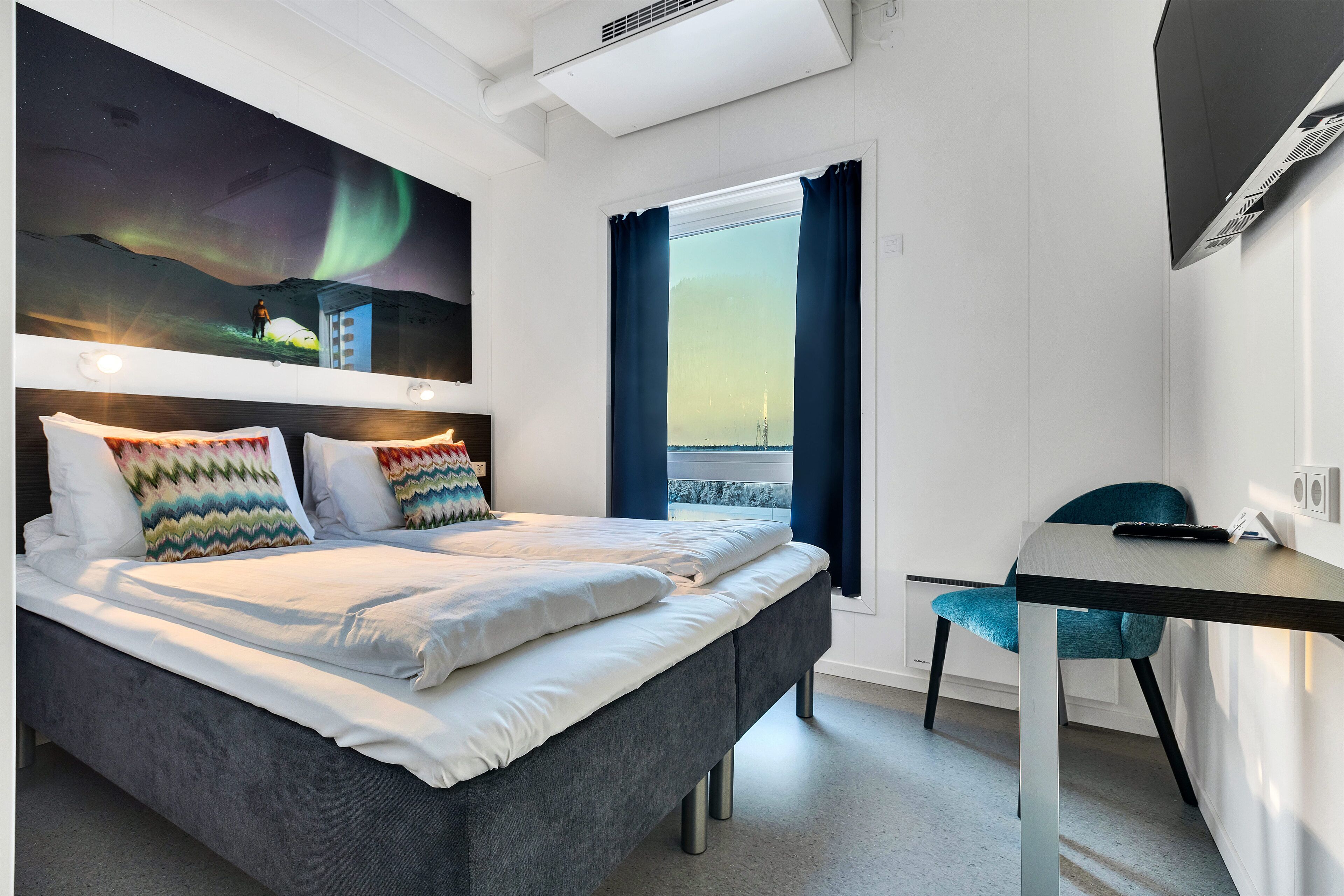 A modern hotel room with a bed, a desk, and a window with curtains.
