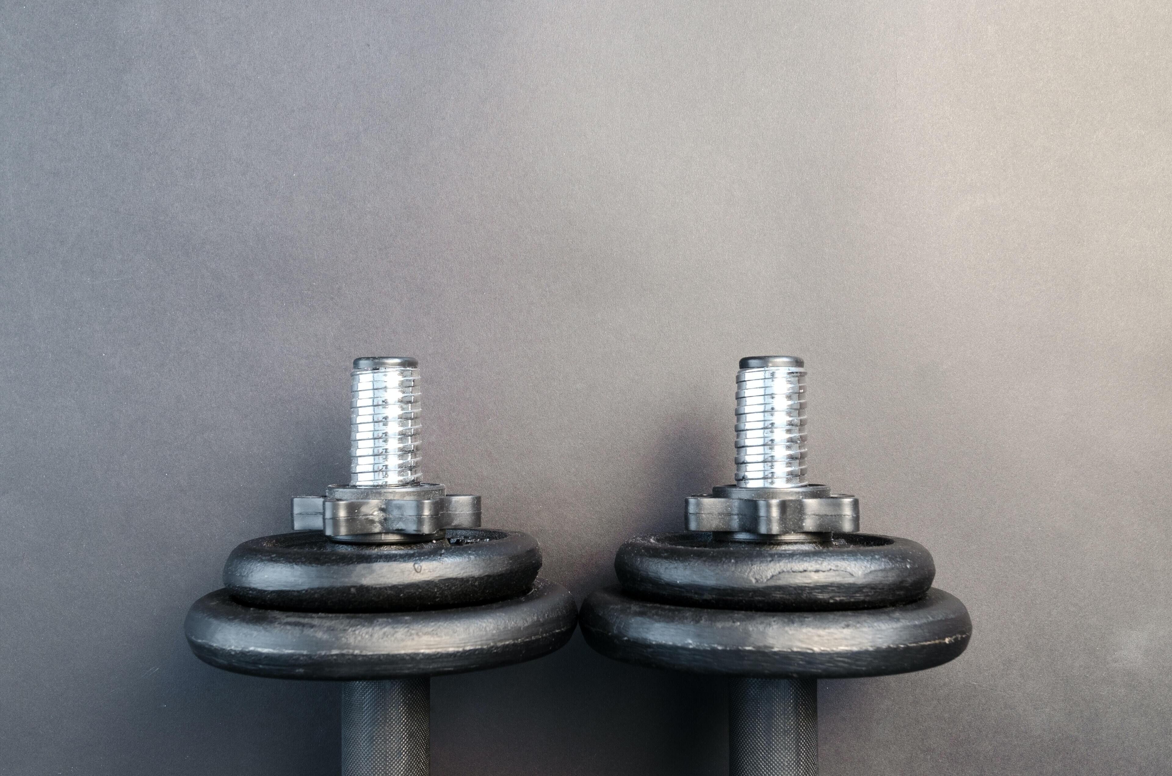 Two black dumbbells with silver weights and a textured grip against a grey background.