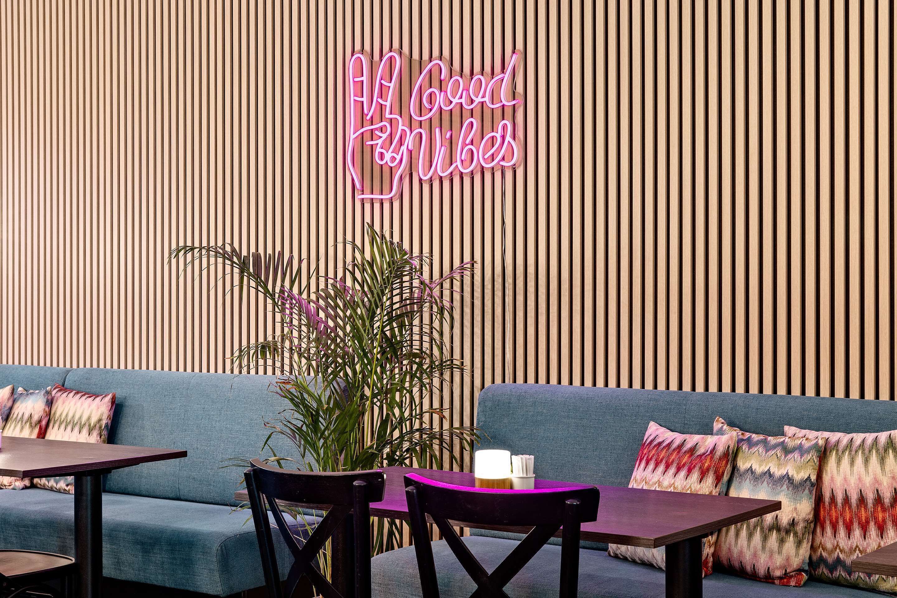 Un espace de détente moderne avec un panneau lumineux au néon, un canapé bleu et un mur à lattes de bois.