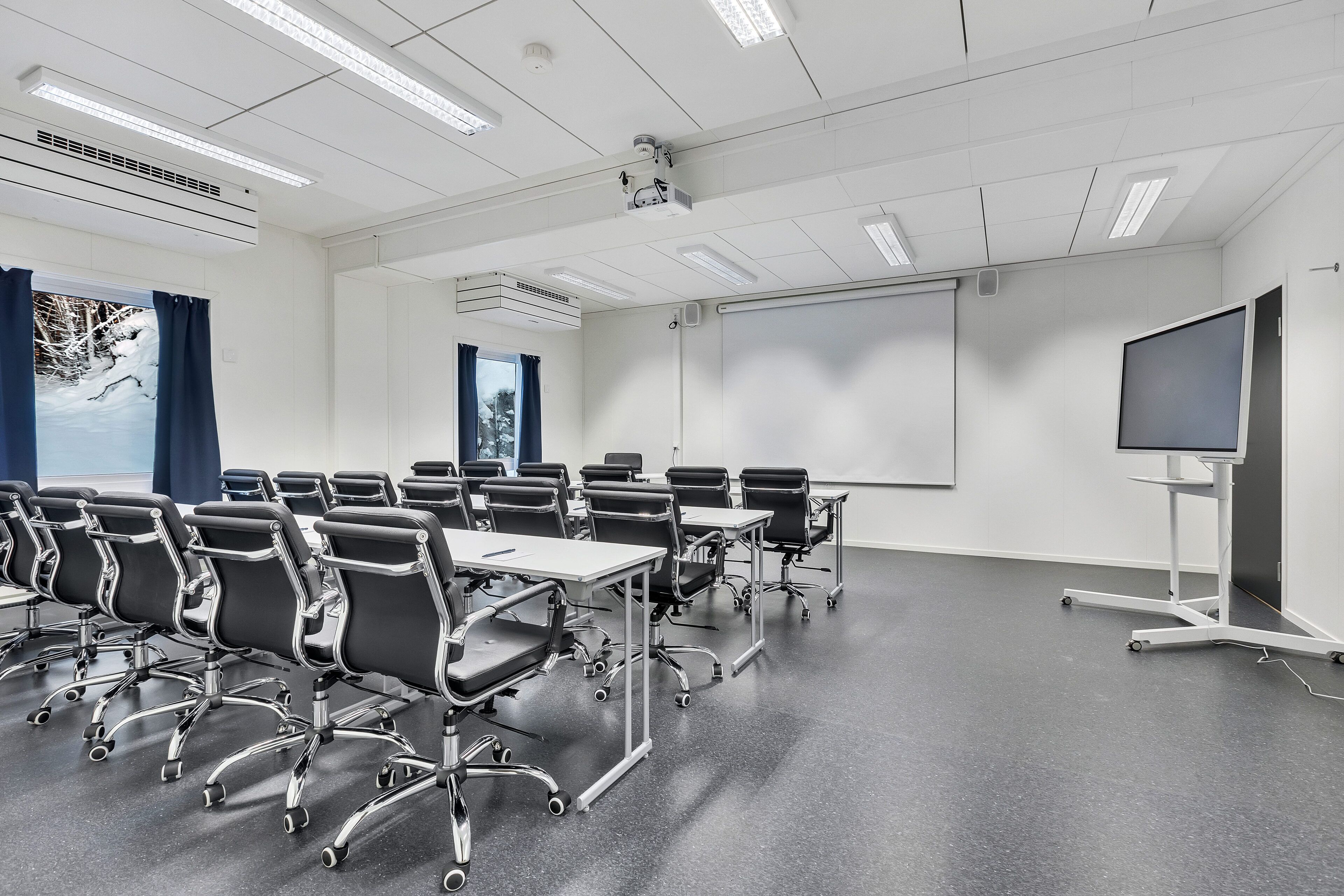 A conference room with rows of black chairs, a large whiteboard, a projector, and a screen.