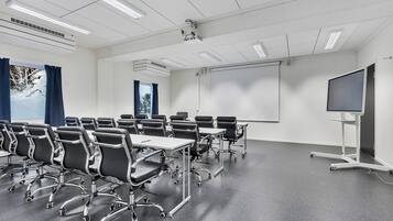 A conference room with rows of black chairs, a large whiteboard, a projector, and a screen.