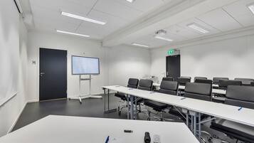 Uma sala de conferências com uma mesa comprida, cadeiras, uma tela de projetor e um quadro branco.