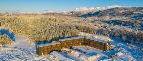 A large, multi-story hotel with a central courtyard, surrounded by snow-covered forest and mountains.
