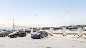 A parking area with electric vehicles and charging stations, a snowy landscape, and a clear sky.