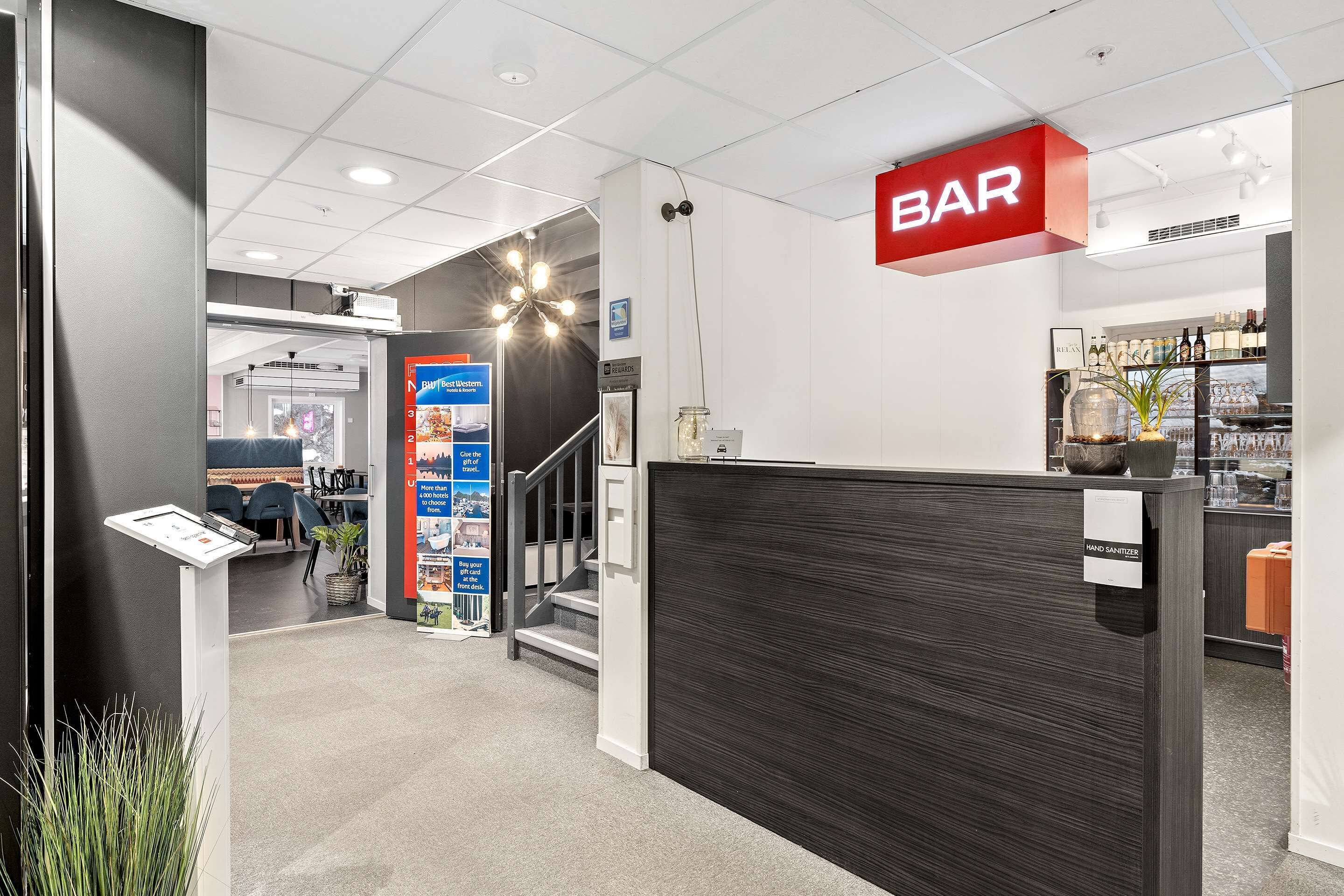 A modern interior with a bar area, a reception desk, and a staircase leading to another level.