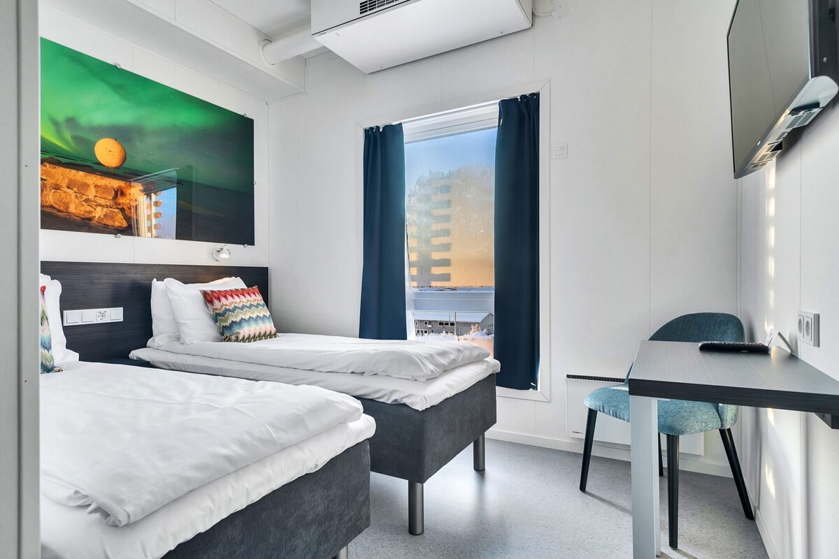 A modern hotel room with two beds, a desk, and a large window with curtains.