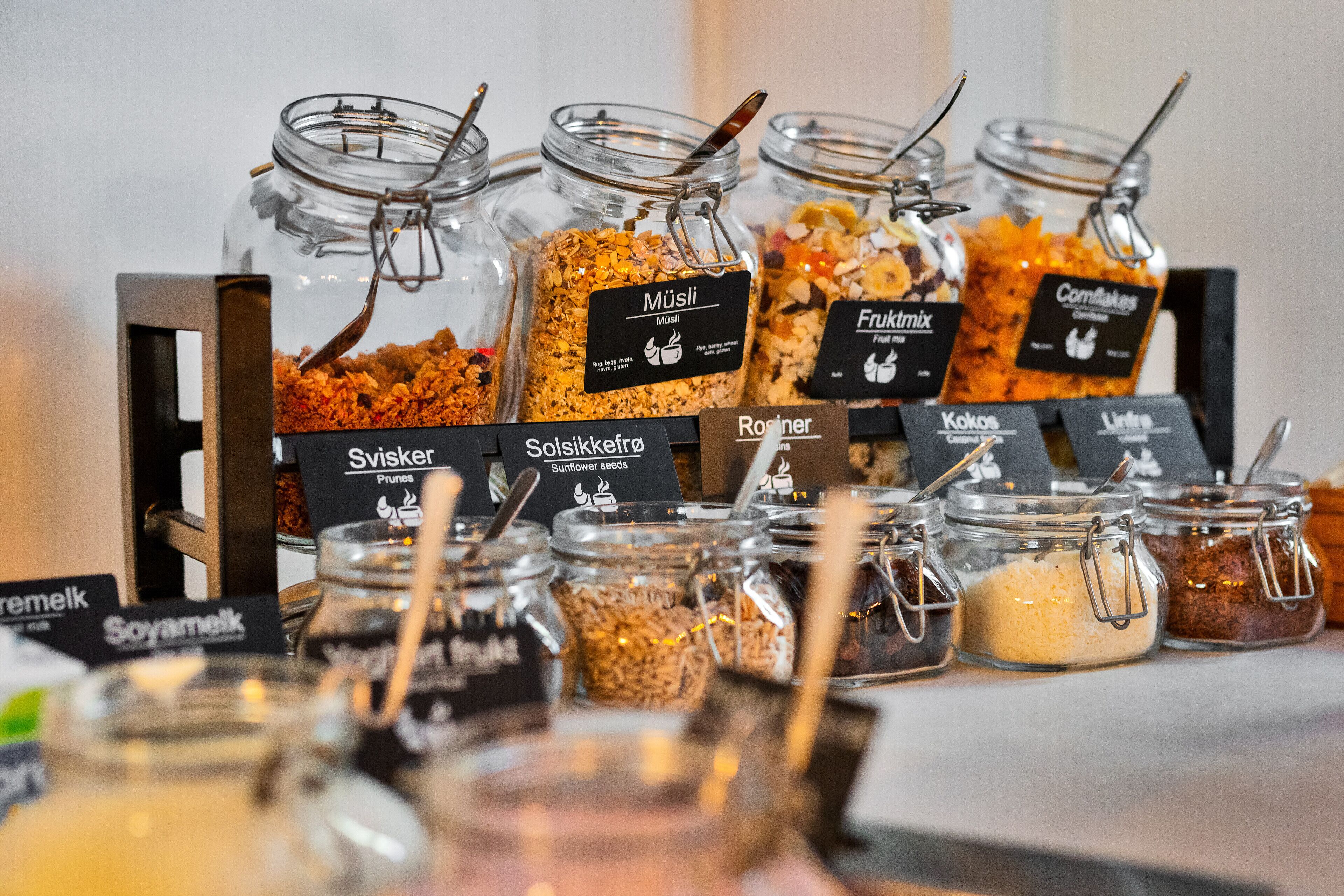 A variety of food items in glass jars with labels, including 'Müsli', 'Solsikkekrotta', 'Röiner', 'Kokos', and 'Lintra'.