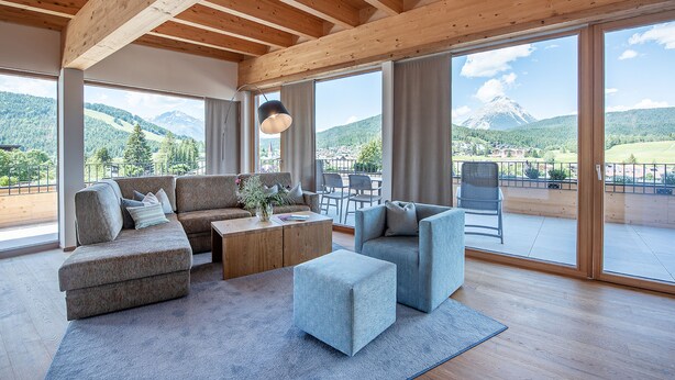 Un salon spacieux doté d’un plafond en bois, de grandes fenêtres offrant une vue sur les montagnes, d’un ensemble de canapés et d’une table basse.