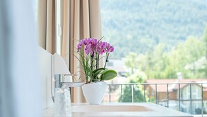 Une salle de bain avec vue sur les montagnes, un lavabo blanc et un vase rempli de fleurs violettes.