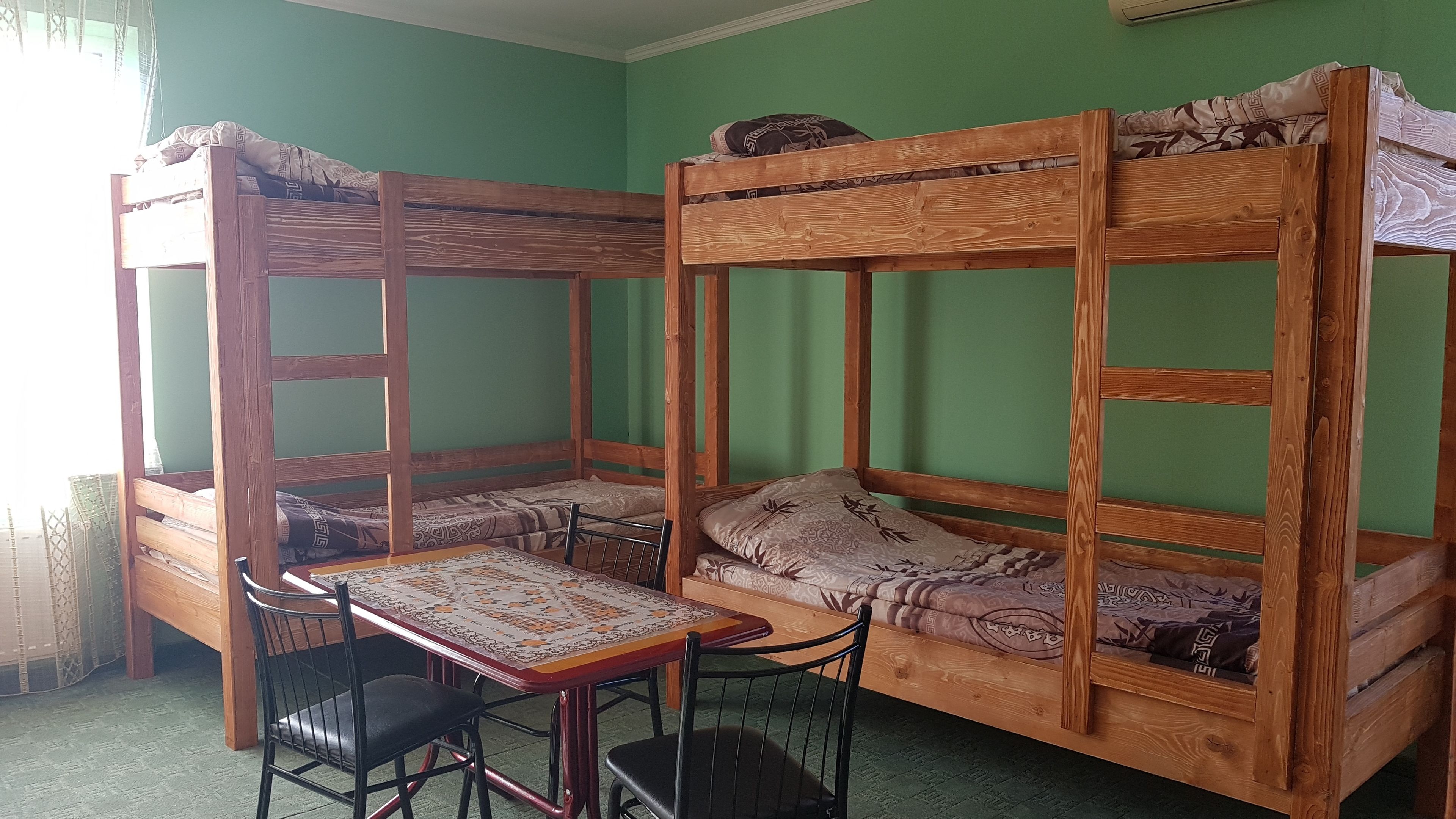 A bunk bed room with a table and chairs, green walls, and a window.