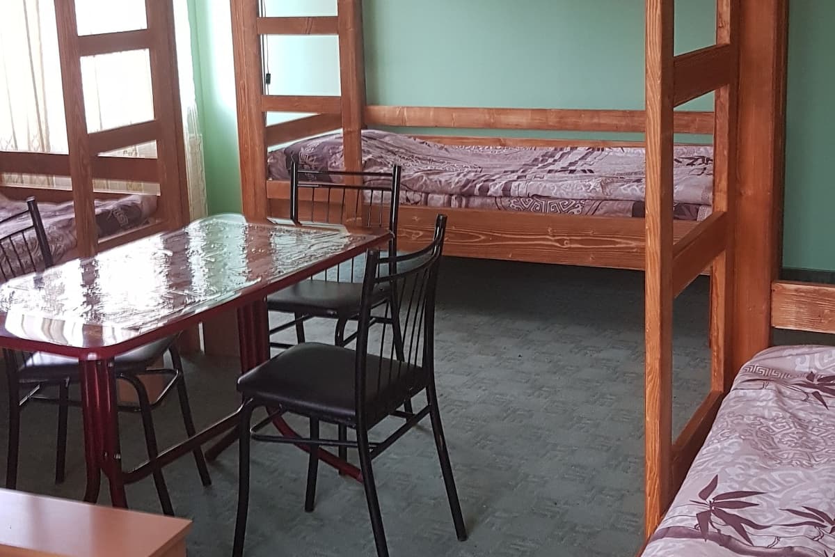 Una habitación con literas, una mesa de madera con sillas y una colcha estampada.