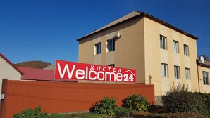 Un edificio con un letrero rojo que dice "Welcome24" y fachada color beige.
