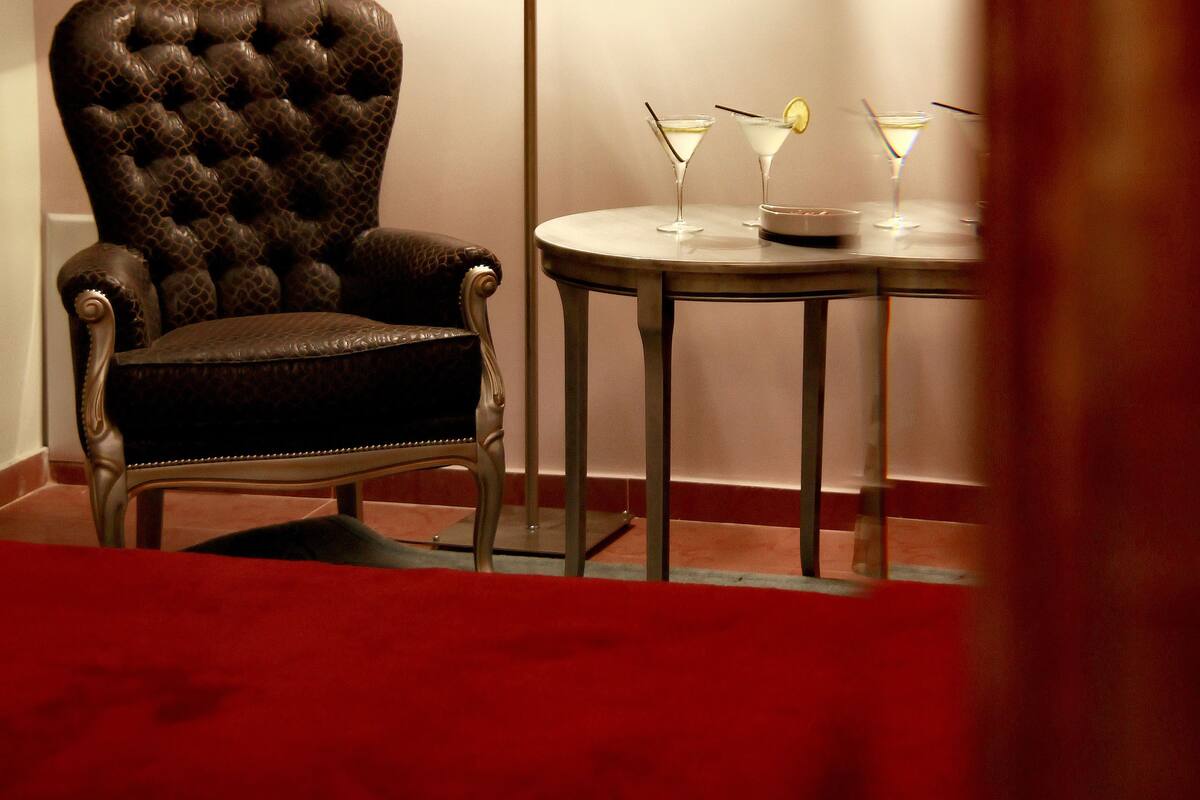 A room with a tufted leather armchair, a round table with two martini glasses, and a wall-mounted light fixture.