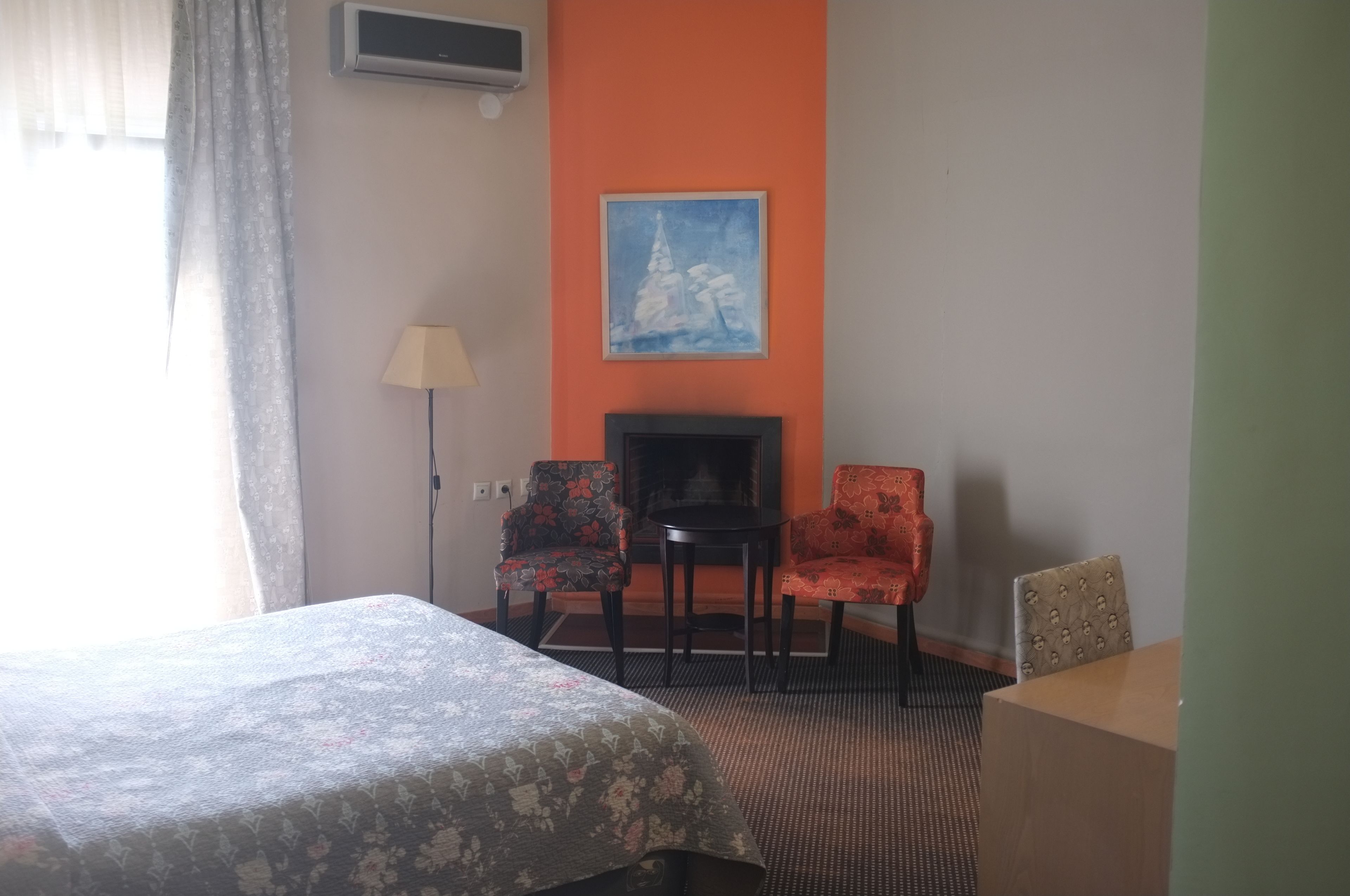 A hotel room with a bed, two chairs, a small table, a lamp, and a painting on the wall.