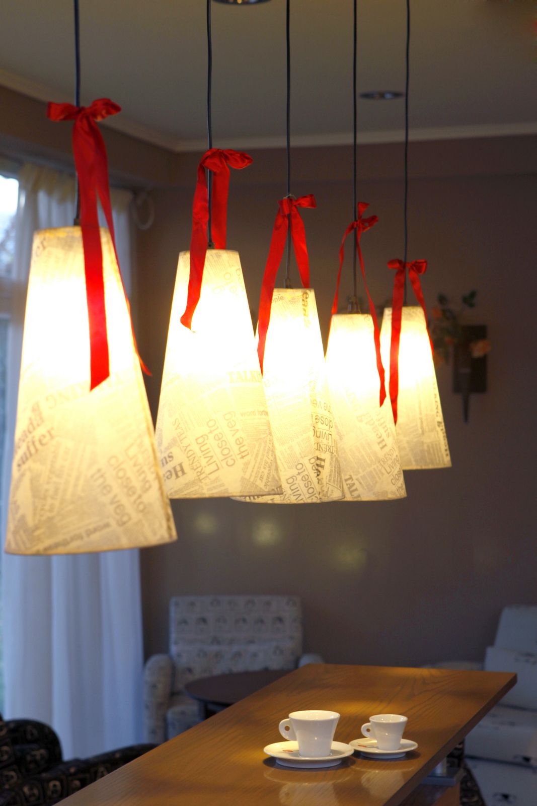 A dining area with a wooden table, two white cups, and a red ribbon chandelier.
