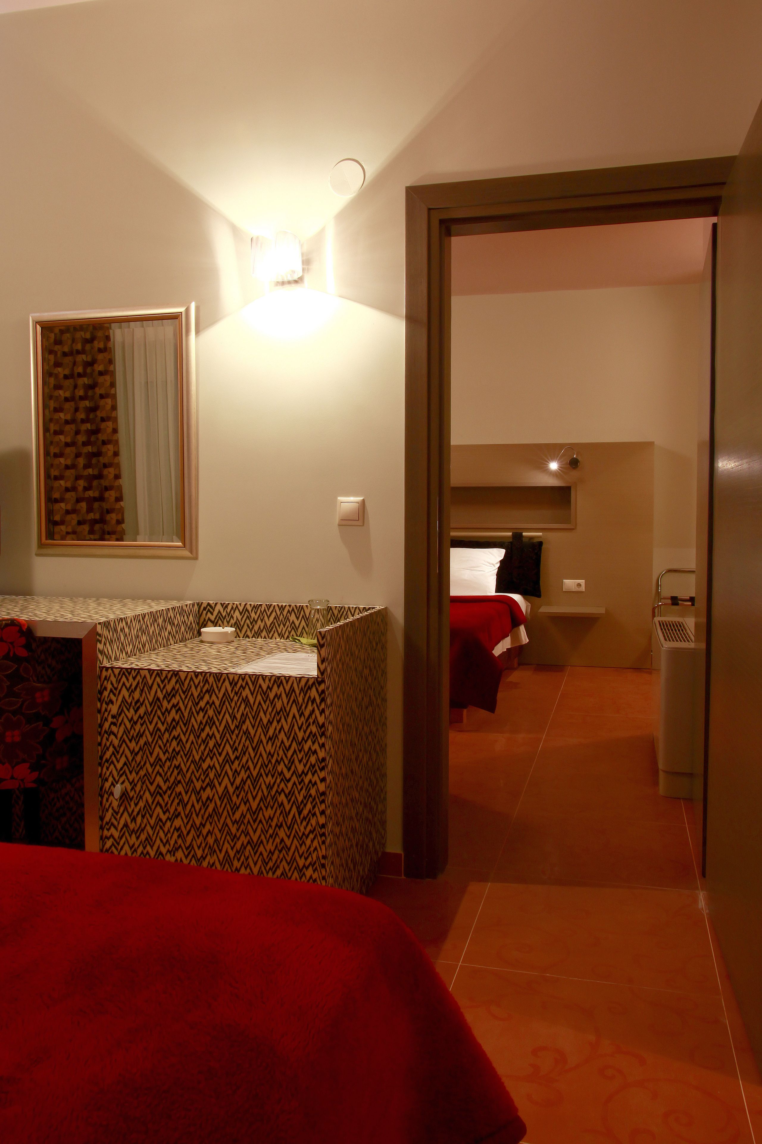 A hotel room with a bed, a small desk, a mirror, and a bathroom visible through an open door.