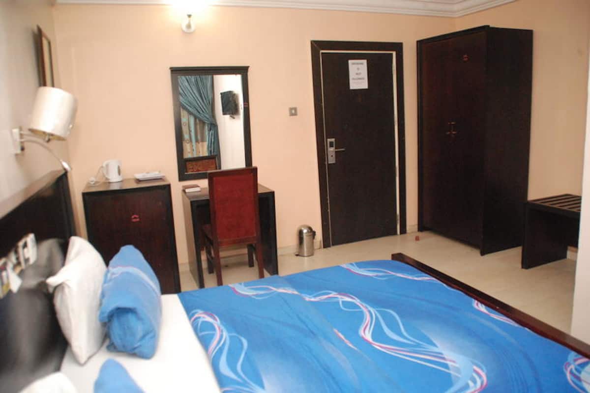 A hotel room with a bed, a desk, a chair, a wardrobe, and a mirror.