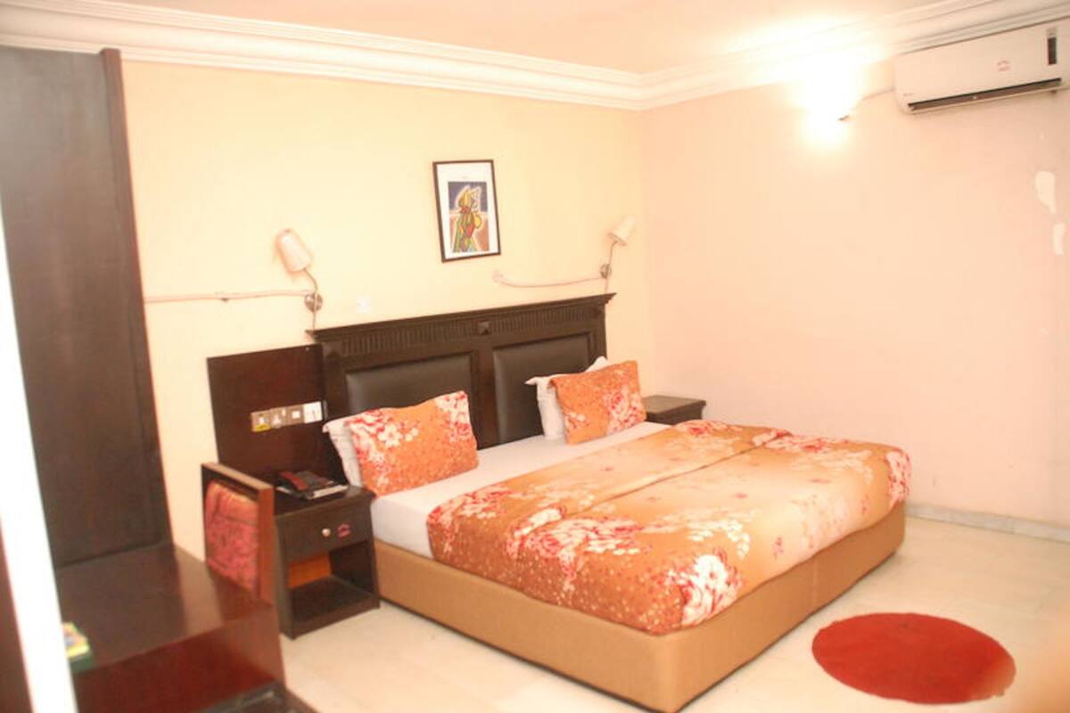 A bedroom with a bed, bedside tables, a nightstand, a wall-mounted air conditioner, and a framed picture above the bed.