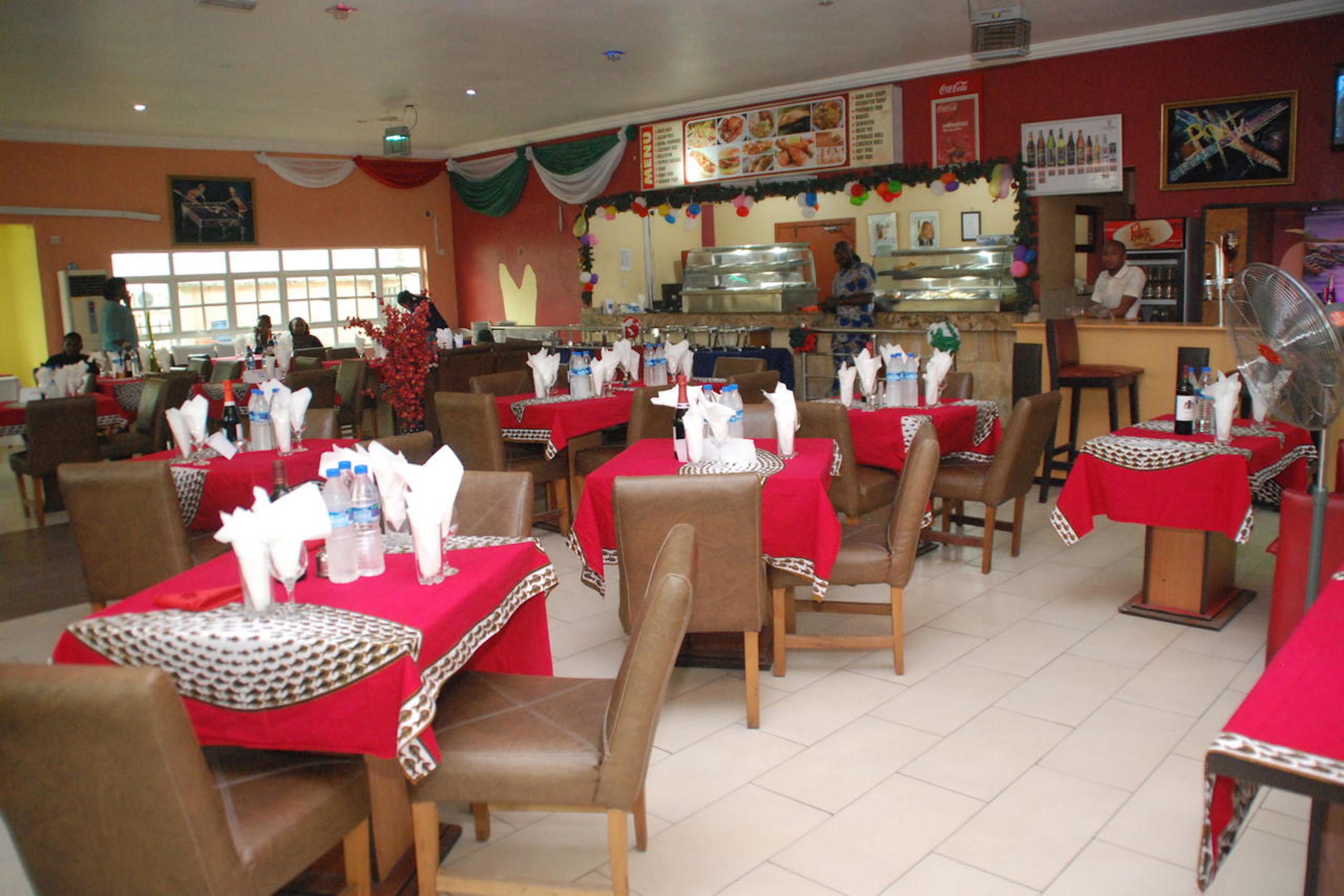 A restaurant with multiple tables covered in red tablecloths, arranged in a spacious layout with chairs.