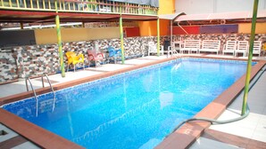 Una piscina interior con solárium de azulejos, un trampolín y una zona de estar cubierta con sillas.