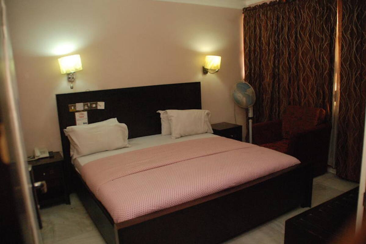 A hotel room with a bed, two bedside lamps, a nightstand, a chair, and a curtain.
