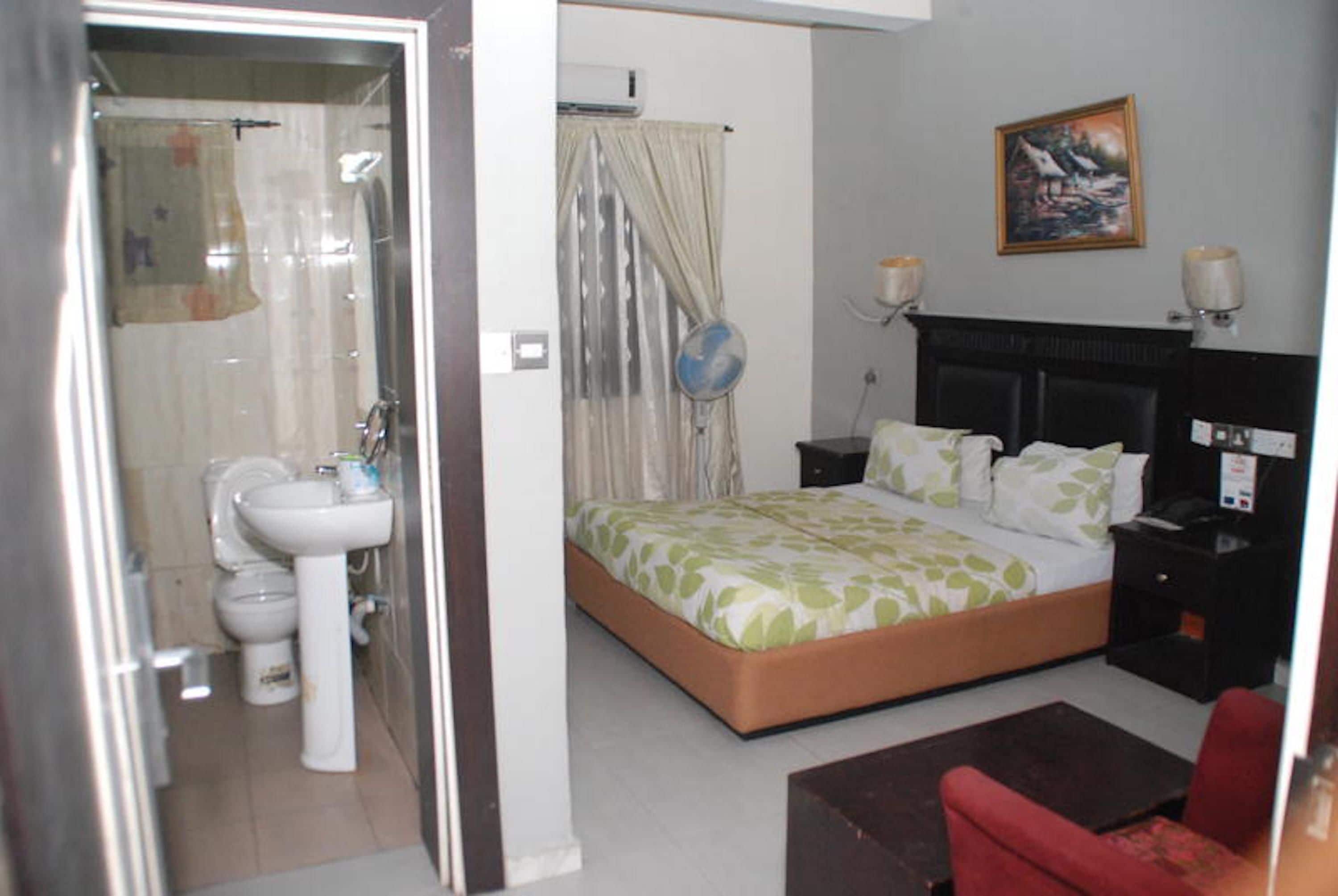 A hotel room with a bed, bedside table, lamp, and a painting on the wall.